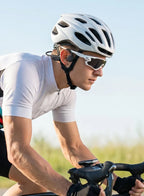 A close-up lifestyle shot of a cyclist wearing a white cycling jersey, a white helmet, and white sunglasses while riding a road bike outdoors.