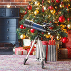 CelesView Telescope on a tripod in front of a decorated Christmas tree with presents underneath.