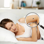 Woman lying on a bed with a magnifying glass inspecting a tattoo on her arm.
