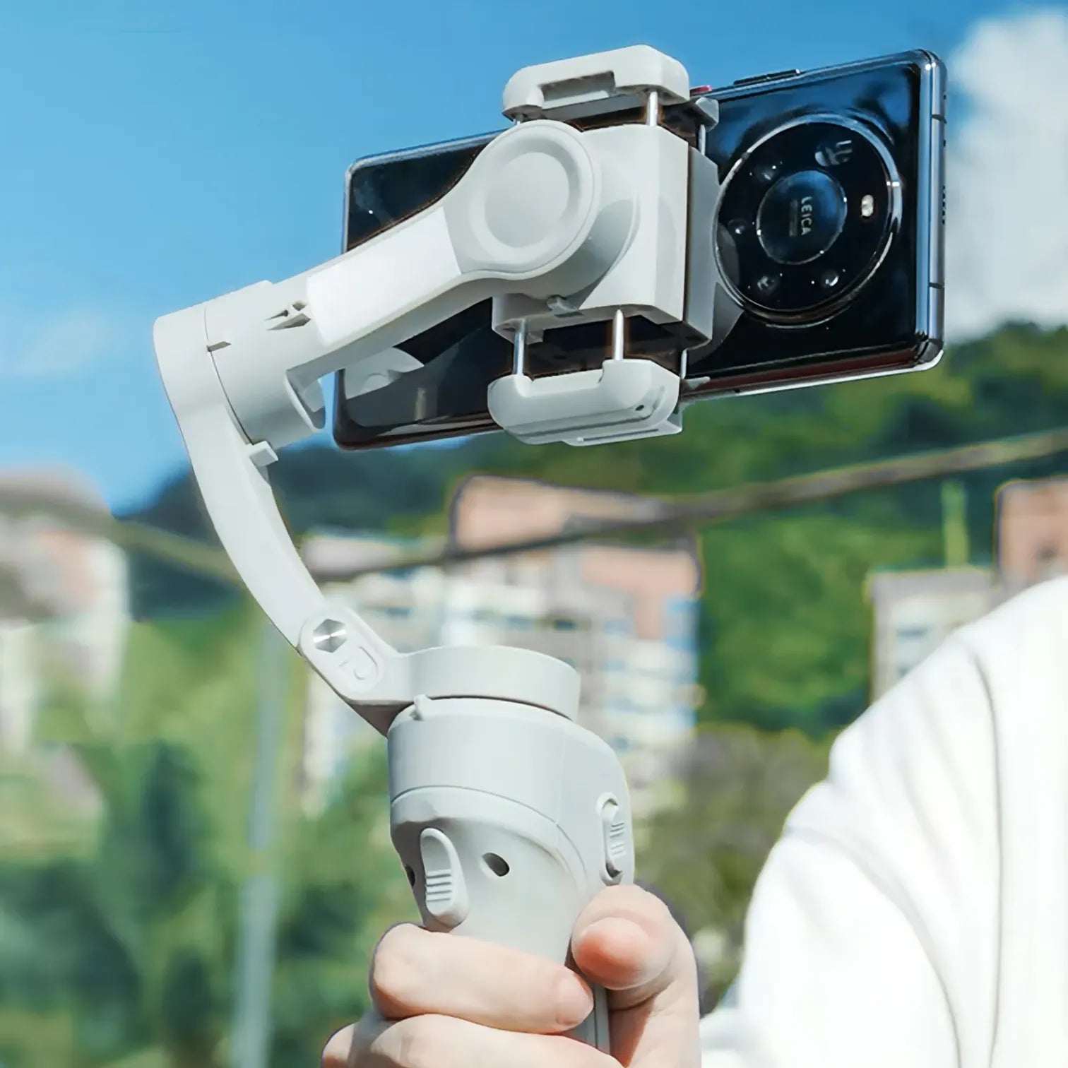 Hand holding a smartphone Kozenix Gimbal with a clear sky and blurred background