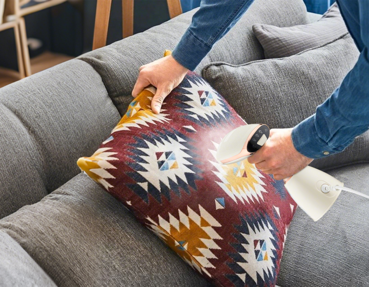 Person using a Meacode Steamer on a decorative pillow on a gray couch.