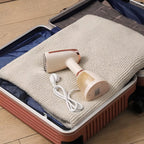 Nordzens Garment Steamer with cord on a blanket inside an open suitcase on a wooden floor