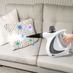 Person using a Oliventa Handheld Steam Cleaner on a pillow on a couch
