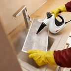 Person Oliventa Handheld Steam Cleaner a kitchen filter with a steam cleaner and yellow gloves.