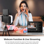 Woman using a webcam setup with a laptop displaying a live stream, on a wooden table.