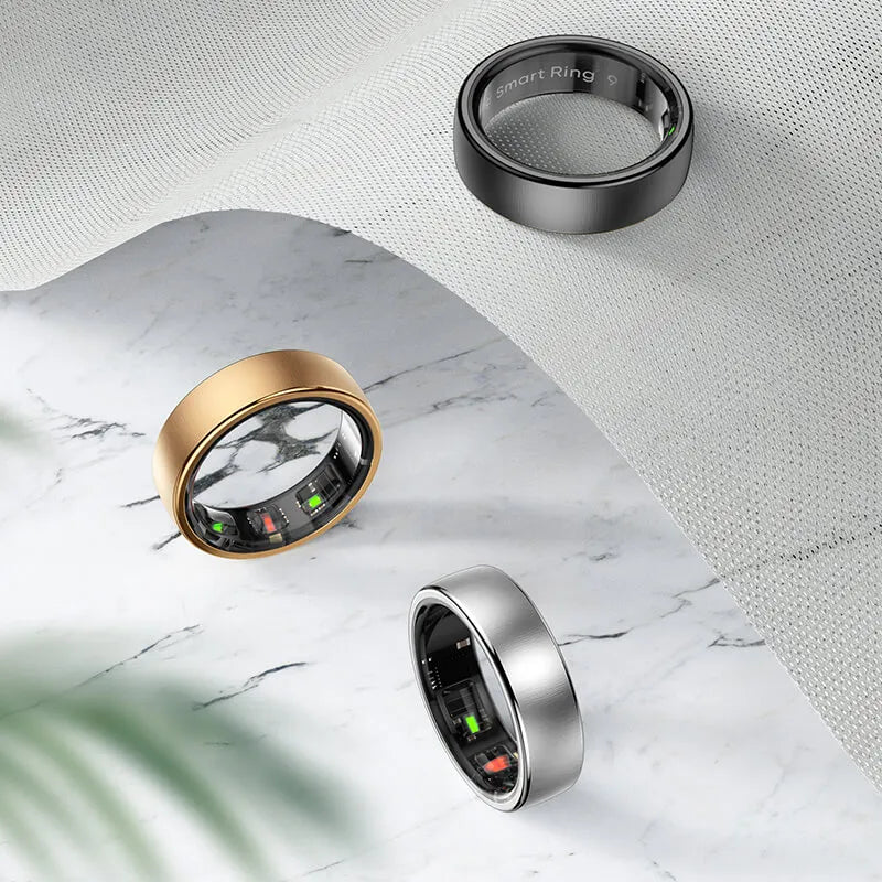 Three Thurgoo Smart Ring in gold, silver, and black on a marble surface with a textured background.