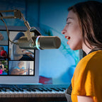 Person speaking into a VIOSBO X1 Microphone in front of a laptop with video calls on screen