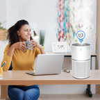 Woman sitting at a desk with a laptop and air purifier, holding a mug.