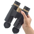 Hand holding a black WildiView Binoculars with gold accents on a white background