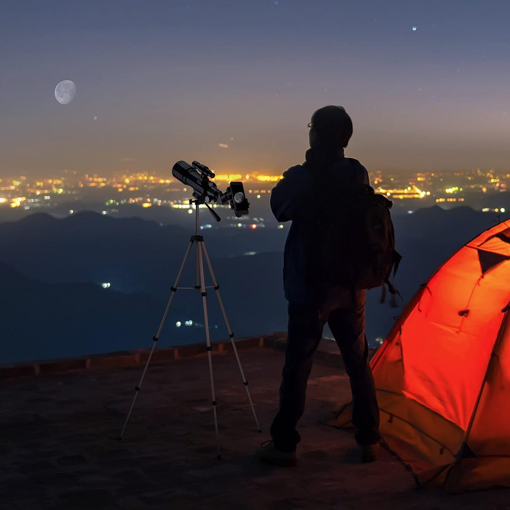 Person with a CelesView Telescope and backpack standing near a tent under a night sky with mountains and city lights.